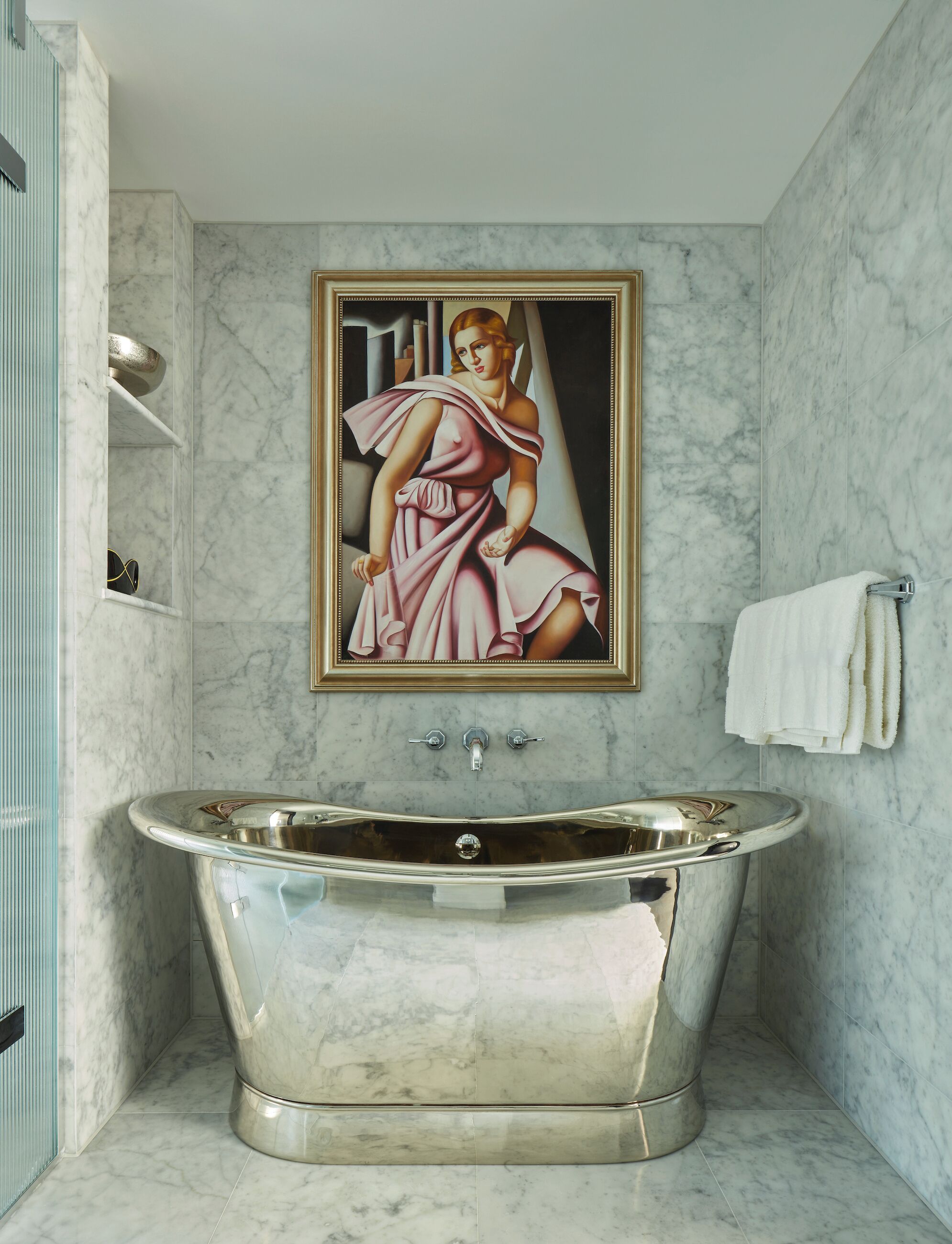 A bathroom with a freestanding bathtub, marble walls, a framed painting, and a towel rack.