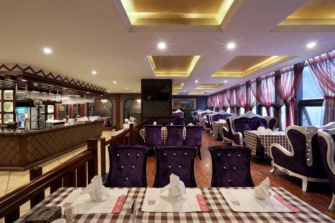 A restaurant with checkered tablecloths, purple upholstered chairs, and a bar area with a counter.