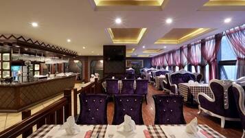 A restaurant with checkered tablecloths, purple upholstered chairs, and a bar area with a counter.