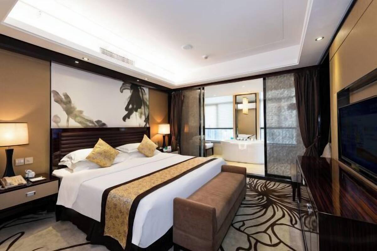 A hotel room with a large bed, bedside tables, a TV, and a bathroom with a bathtub.