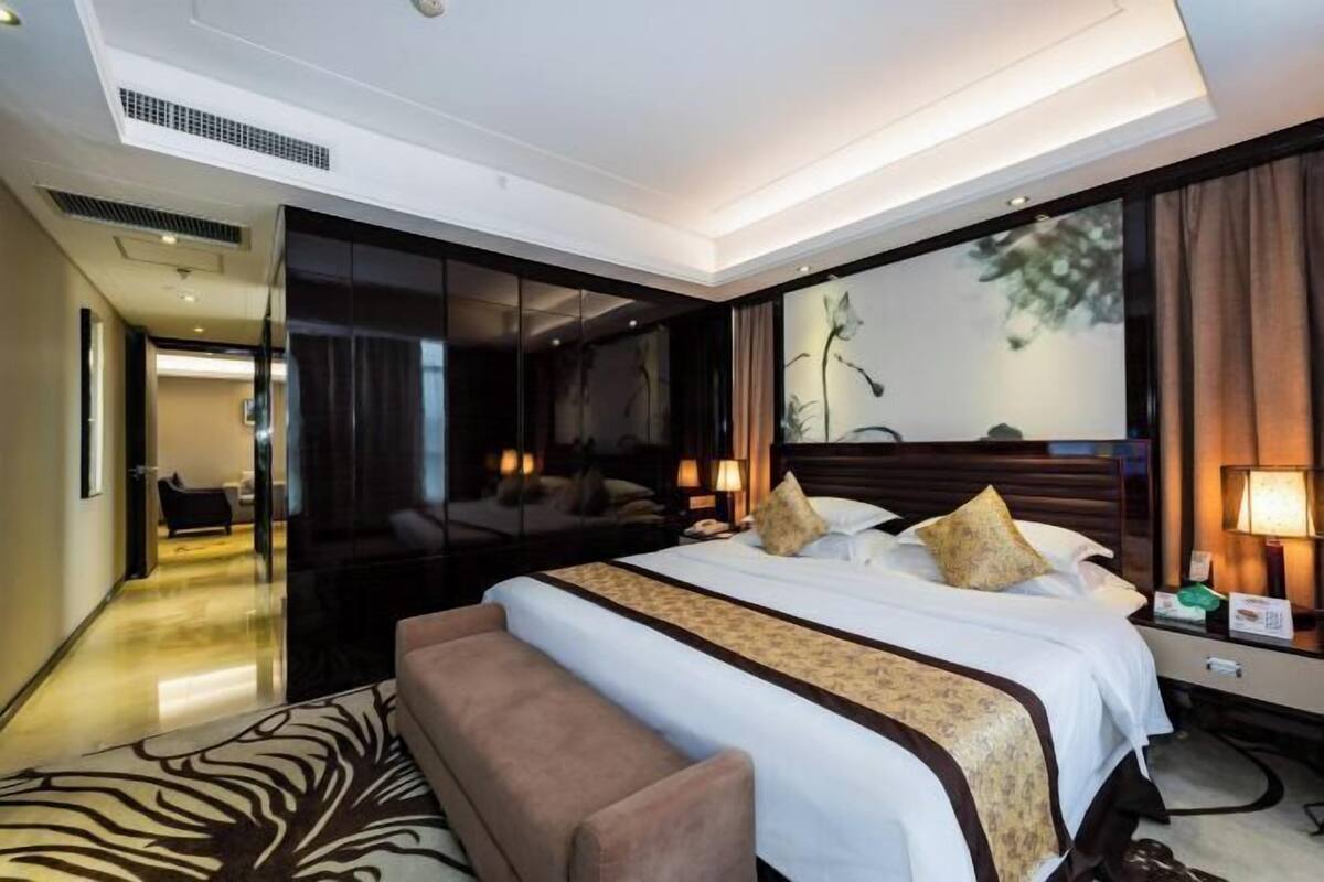 A modern hotel room with a large bed, a sofa, a desk, and a large window with curtains.