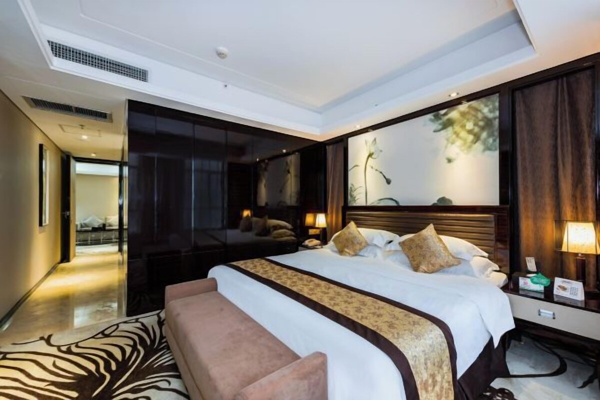 A hotel room with a large bed, a sitting area, a mirror, and a view of the outdoors.