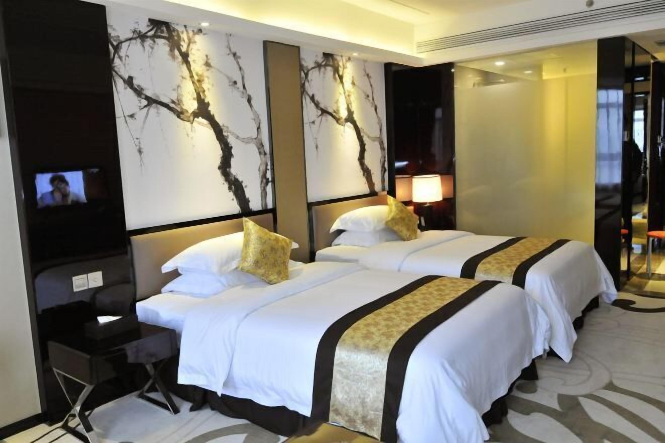 A hotel room with two beds, a desk, and a TV on the left wall.