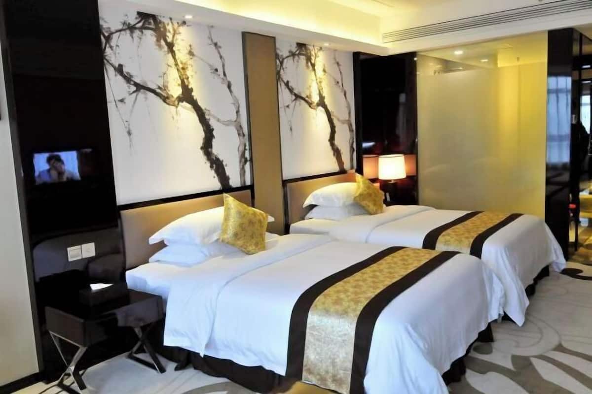 A hotel room with two beds, a TV, a desk, and a wall with a tree design.