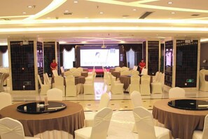 Un salón de conferencias con mesas redondas, sillas blancas y una pantalla grande al frente.