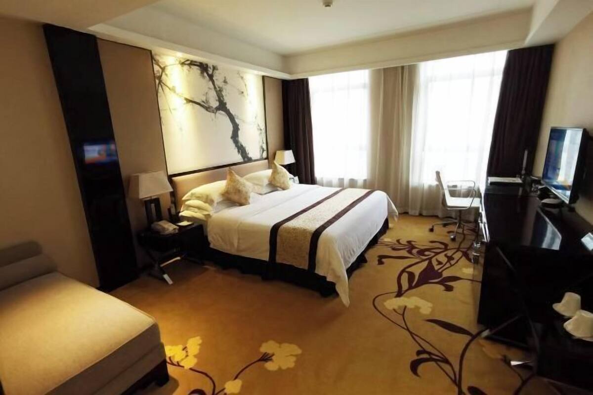 A hotel room with a large bed, a desk with a computer, a TV, and a decorative wall piece.