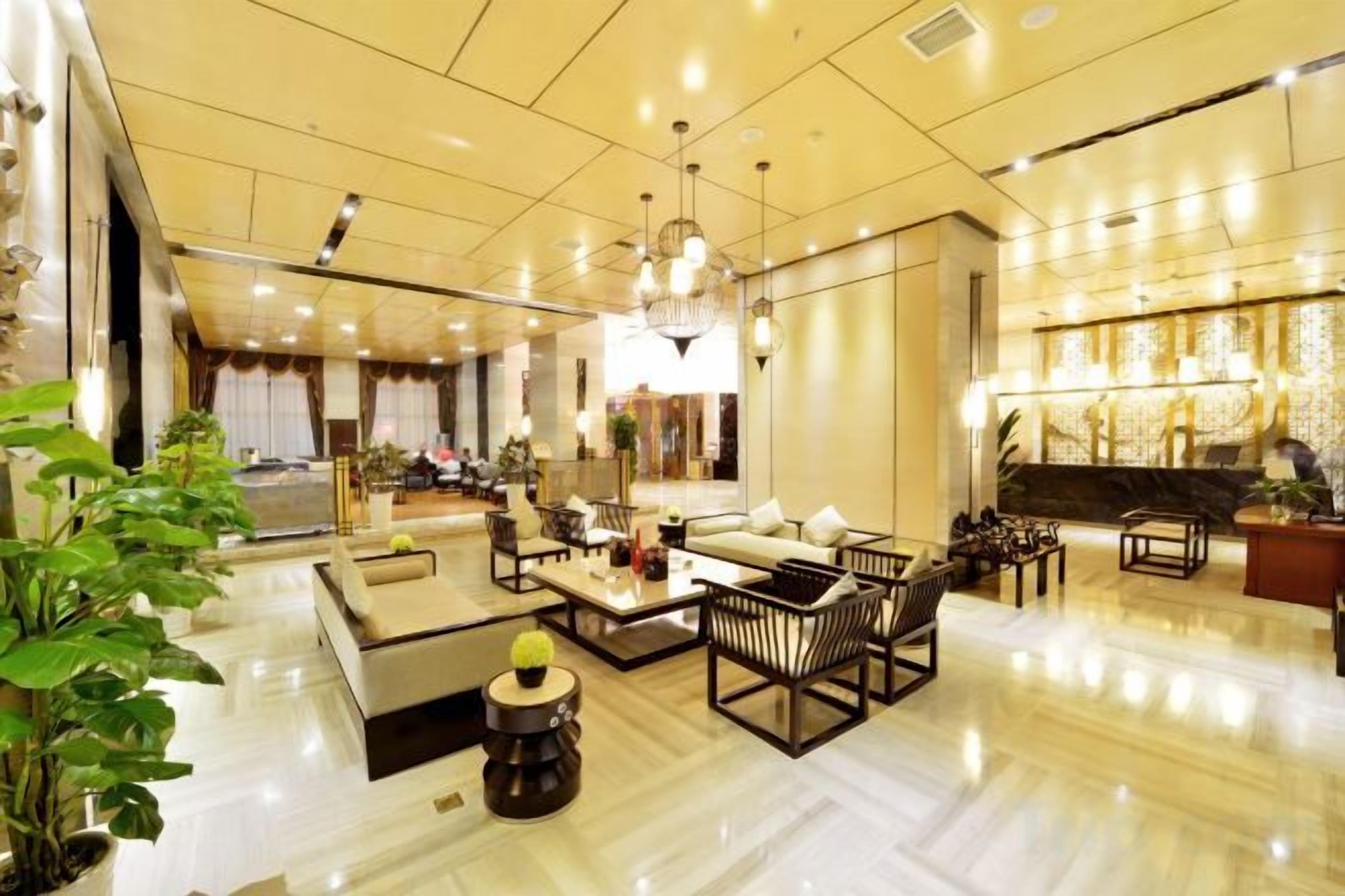 A spacious living area with a large sofa set, a coffee table, and a dining table. There are multiple chairs and a small side table. The room has a high ceiling with recessed lighting and a chandelier.