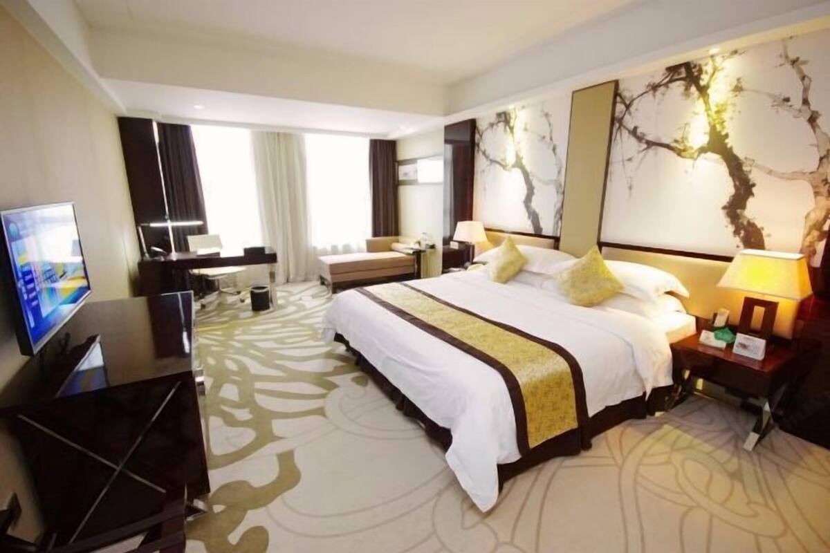 A hotel room with a bed, a desk, a television, and artwork on the walls.