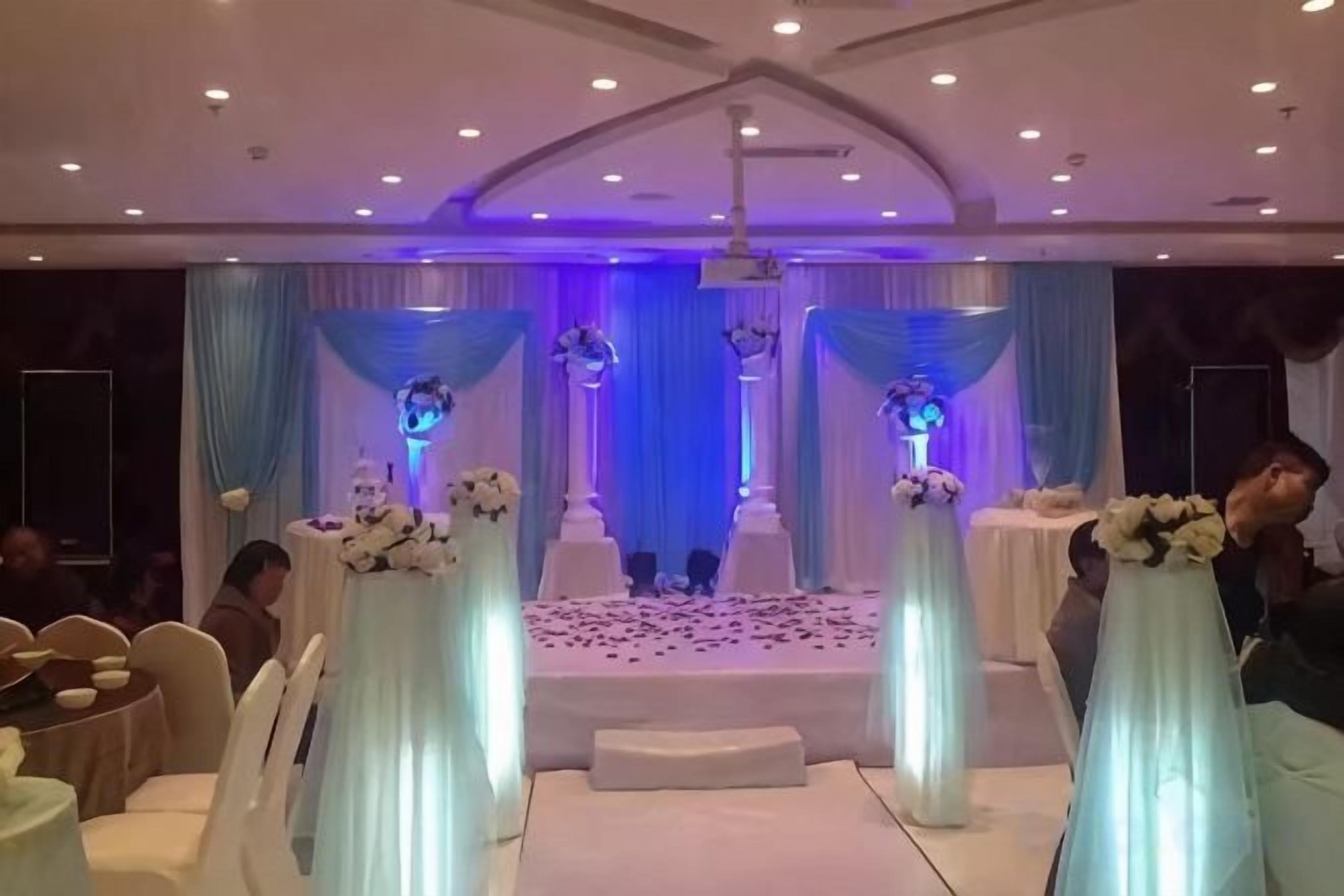 Un espace événementiel intérieur doté d’une scène, de rideaux décoratifs et d’arrangements floraux.