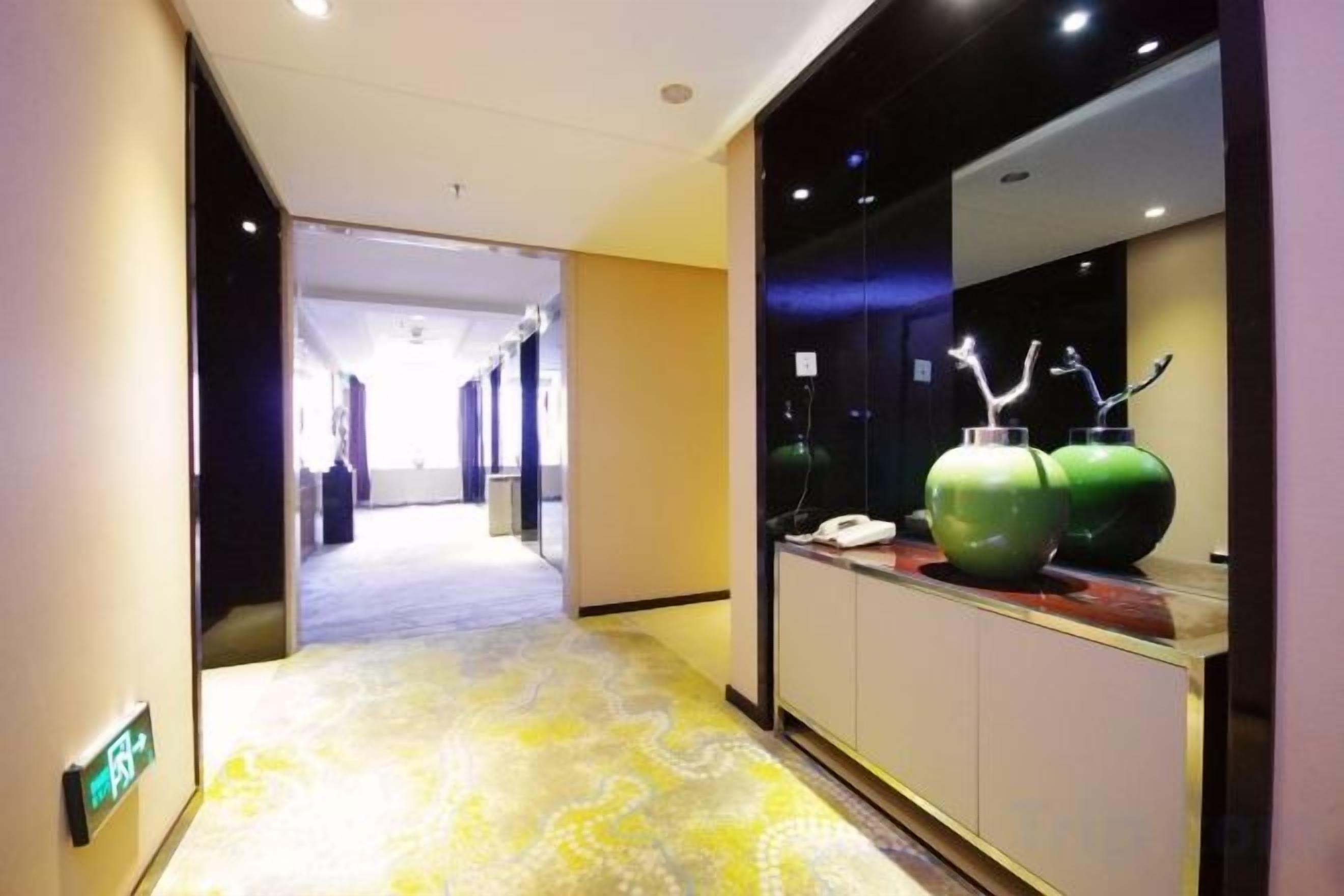 Un pasillo de hotel con alfombra estampada, un mostrador de recepción con un teléfono y un gran jarrón verde sobre el mostrador.
