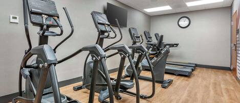 A gym with multiple treadmills arranged in a row, a wall-mounted TV, and a clock.