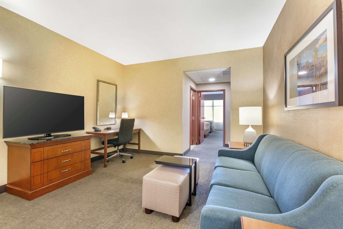 A hotel room with a large flat-screen TV, a wooden dresser, a blue sofa, a small table, and a framed picture on the wall.