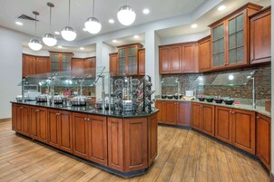Una cocina amplia con armarios de madera, una isla central con encimera de vidrio e iluminación colgante.
