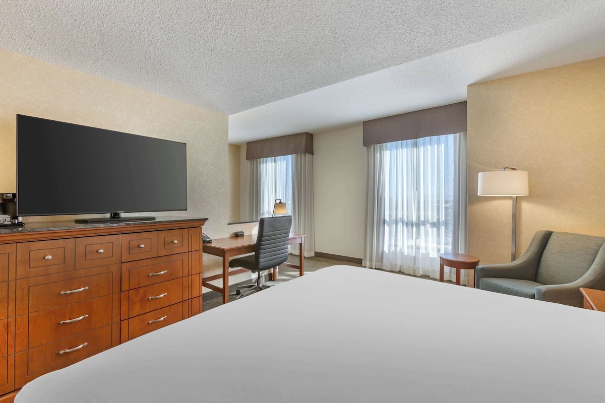 A hotel room with a bed, a desk, a chair, a television, and a lamp.