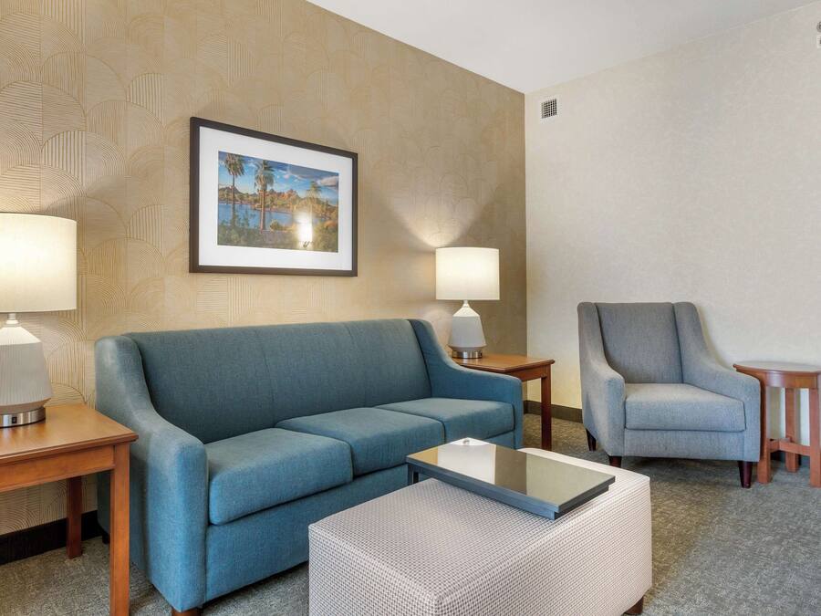 Ein Hotelzimmer mit einem blauen Sofa, einem grauen Sessel, einem kleinen Tisch und zwei Lampen.