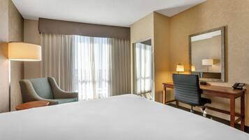Habitación de hotel con una cama grande, dos sillas, un escritorio con una computadora y un espejo.