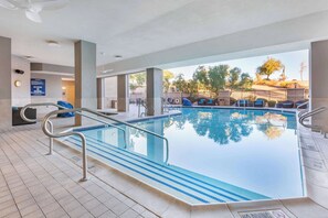 Una piscina interior con agua azul cristalina, suelo de baldosas y vistas al exterior.