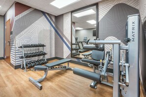 Ett gym med utrustning för styrketräning, hantlar och löpband.