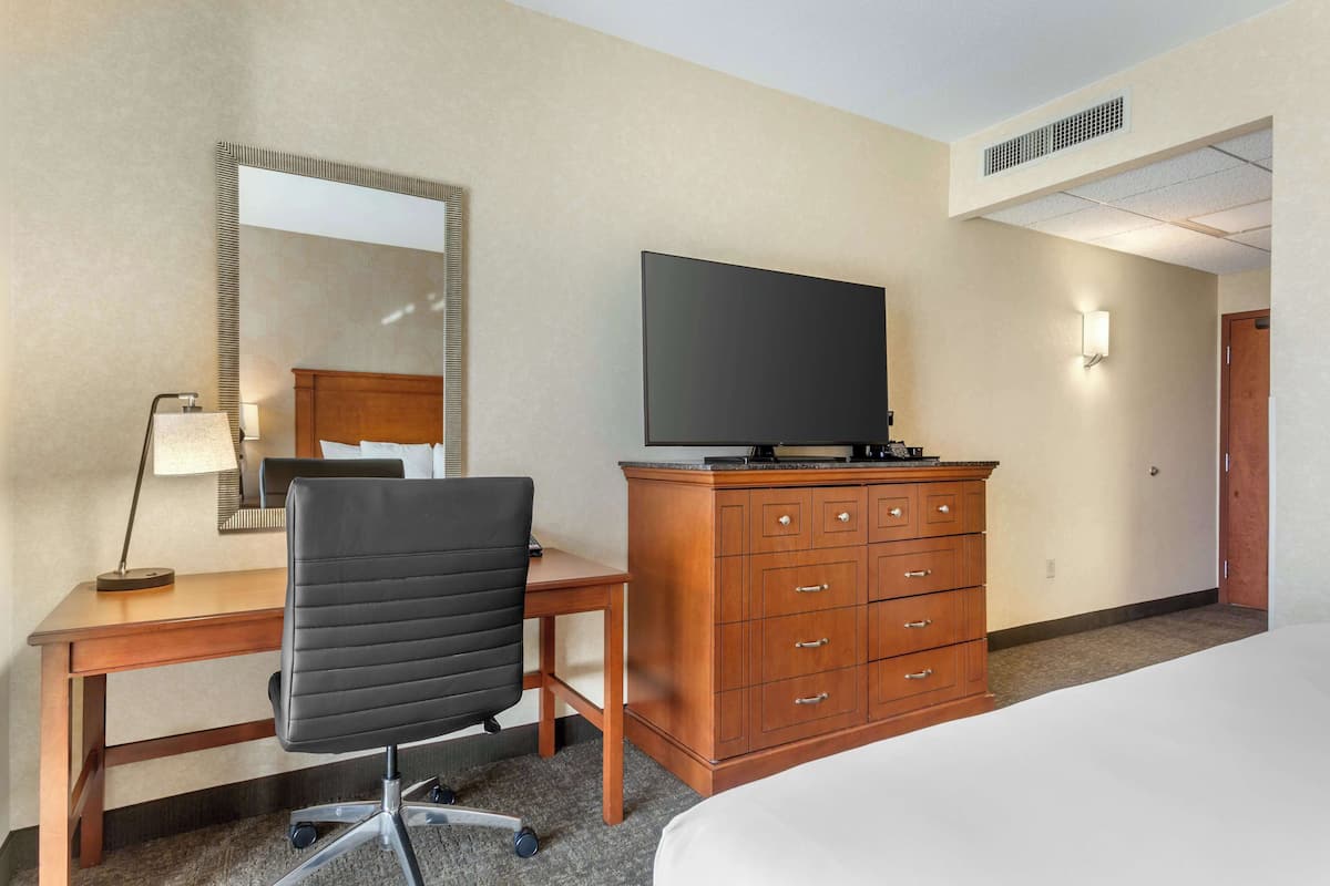 A hotel room with a bed, a desk with a chair, a television, and a wooden dresser.