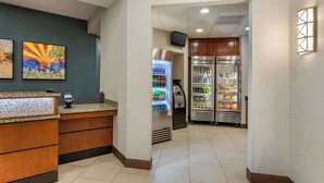A hotel lobby with a reception desk, a refrigerator, and vending machines.