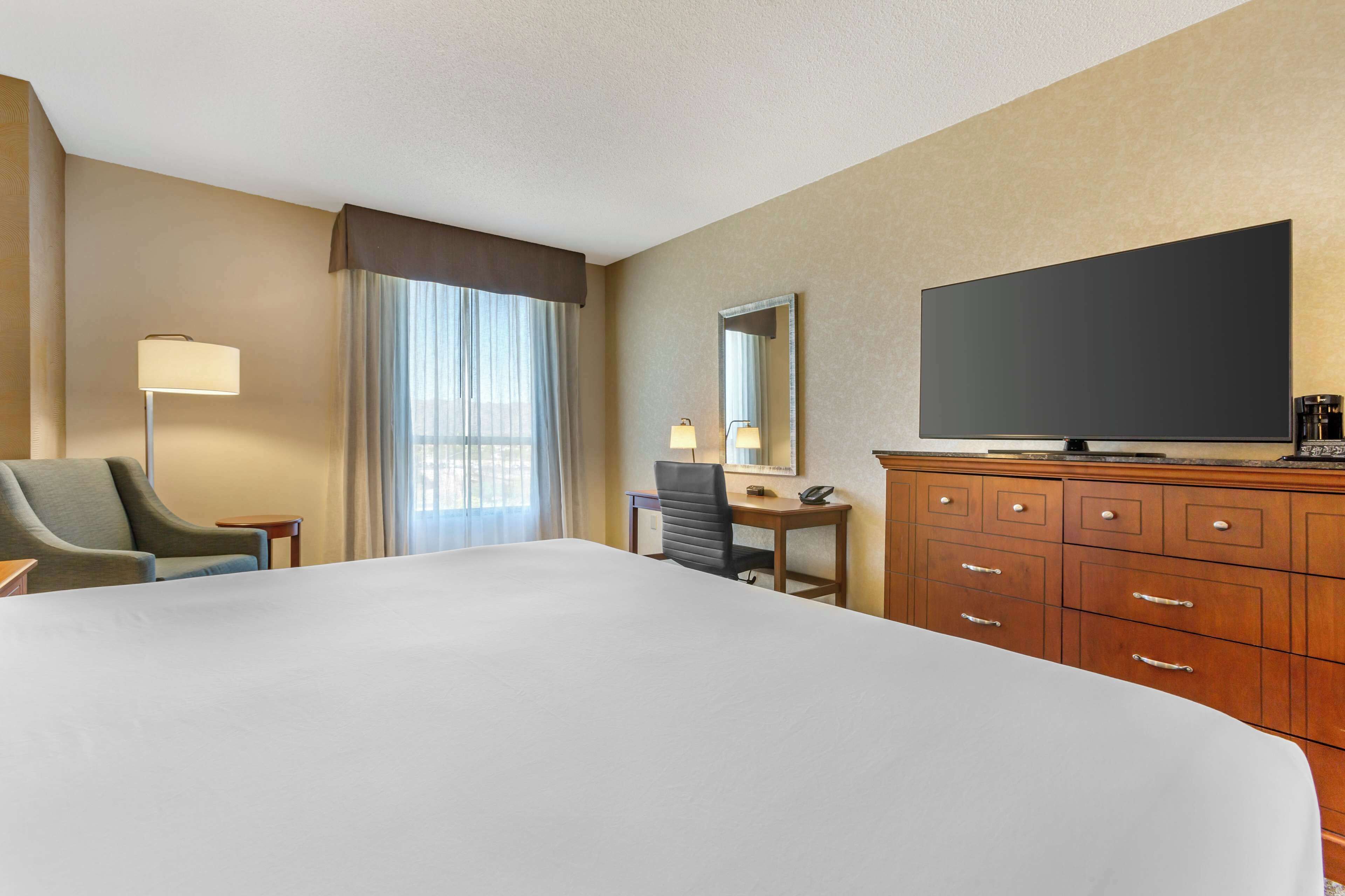 A hotel room with a large bed, a desk with a chair, a television, and a dresser.