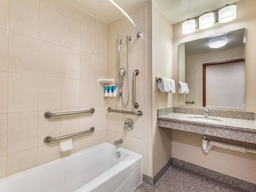 A bathroom with a bathtub, grab bars, a sink, and a mirror.