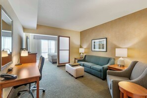 Una habitación de hotel con un escritorio, dos sillones, un sofá, una mesita y una lámpara.