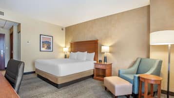 A hotel room with a large bed, a desk, a chair, a small table, and two lamps.