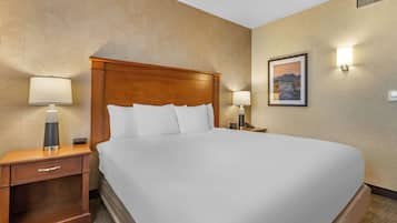 A neatly made bed in a hotel room with a wooden headboard, a nightstand with a lamp, and a wall-mounted picture.