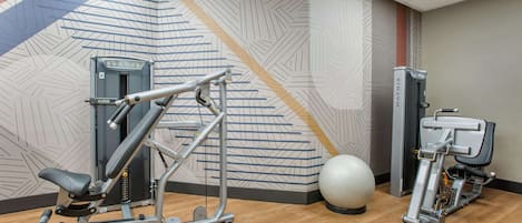 Une salle de sport équipée de matériel d’exercice, un mur orné de motifs géométriques et un grand ballon d’exercice.
