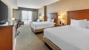 A hotel room with two beds, a desk, a chair, and a television.