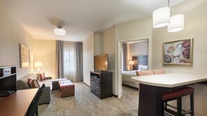 A hotel room with a bed, a desk, a TV, a dining area, and a bathroom. - Staybridge Suites Houston I-10 West-beltway 8 by IHG (Houston)
