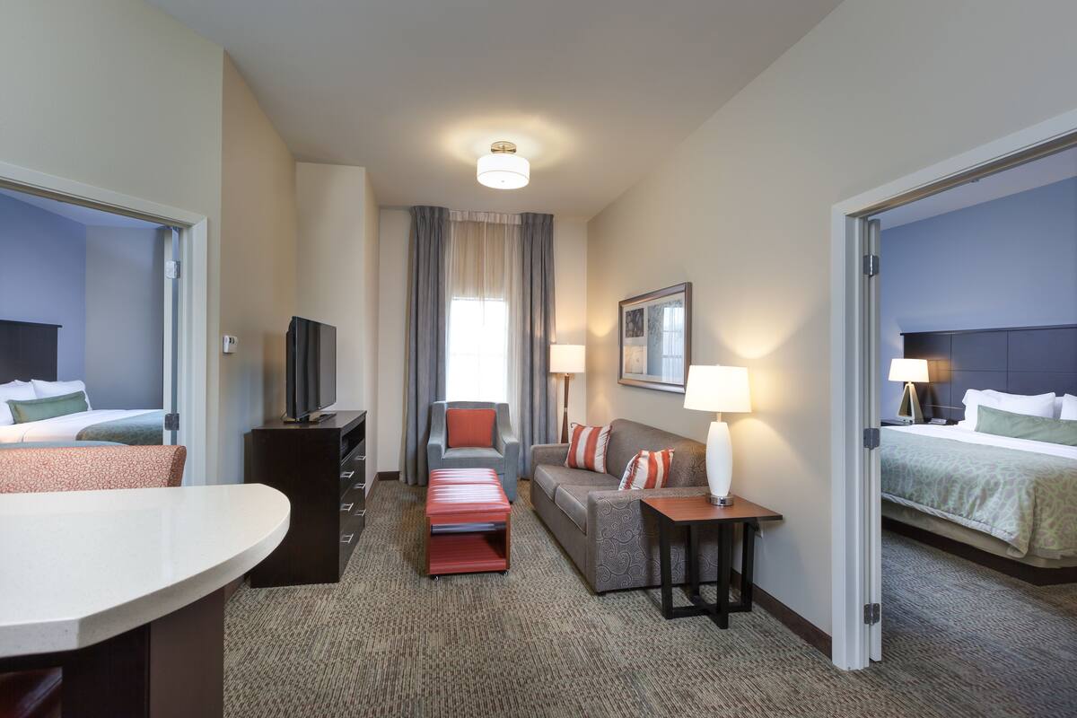 Habitación de hotel con cama, sofá, escritorio, televisor y ventana con cortinas.