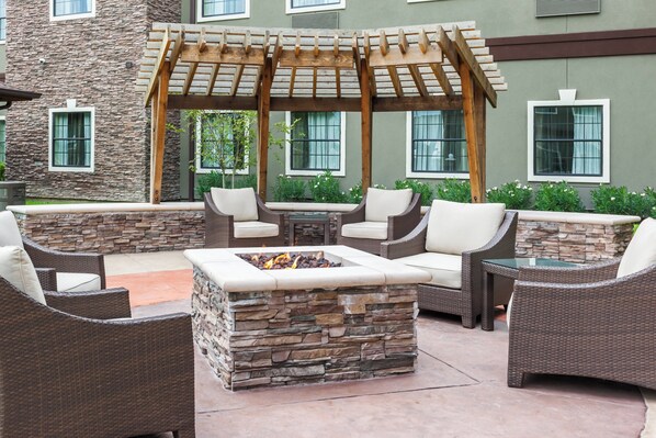 An outdoor patio with wicker furniture, a stone fire pit, and a wooden pergola.