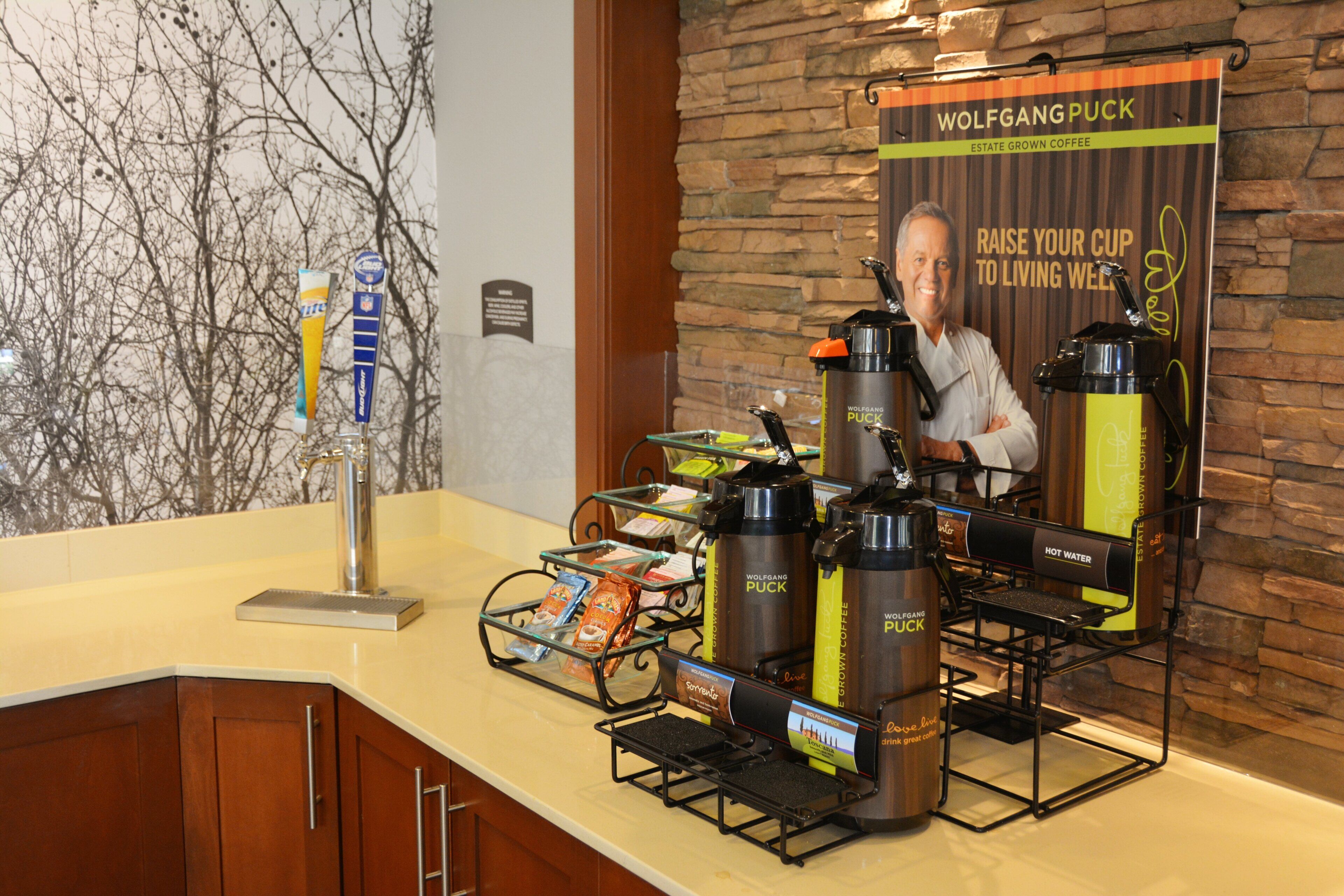 Una estación de café con tazas de marca y un letrero que indica café Wolfgang Puck.