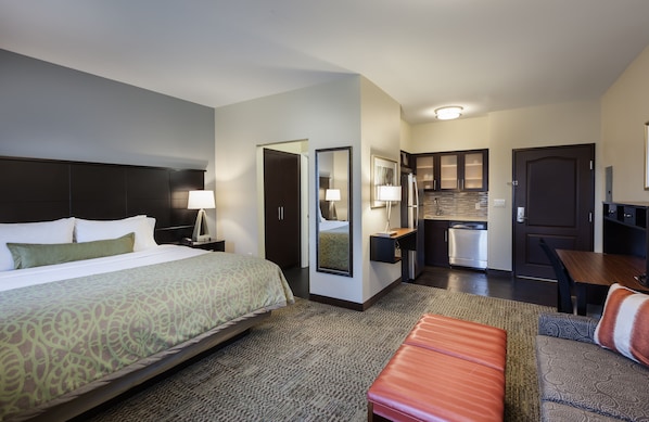 A hotel room with a large bed, a desk, a kitchenette, and a seating area.