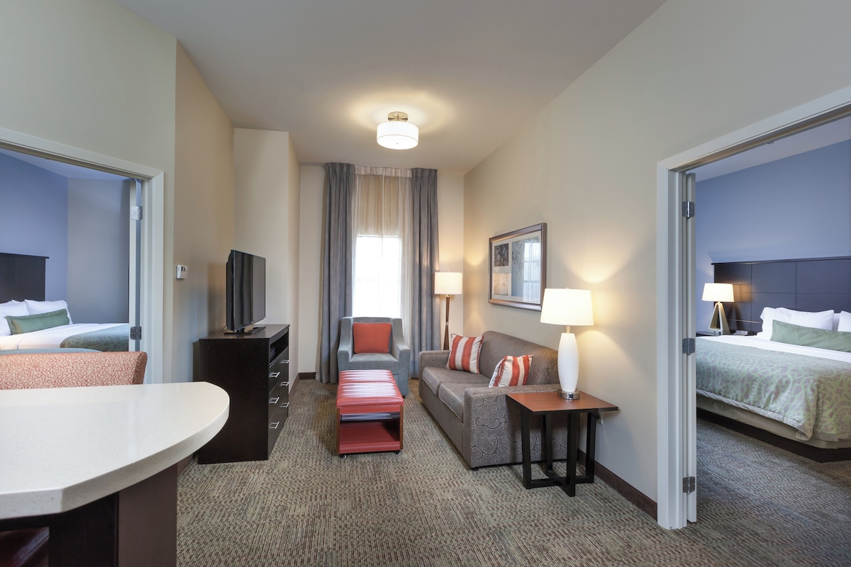 Habitación de hotel con cama, sofá, escritorio, televisor y lámpara.