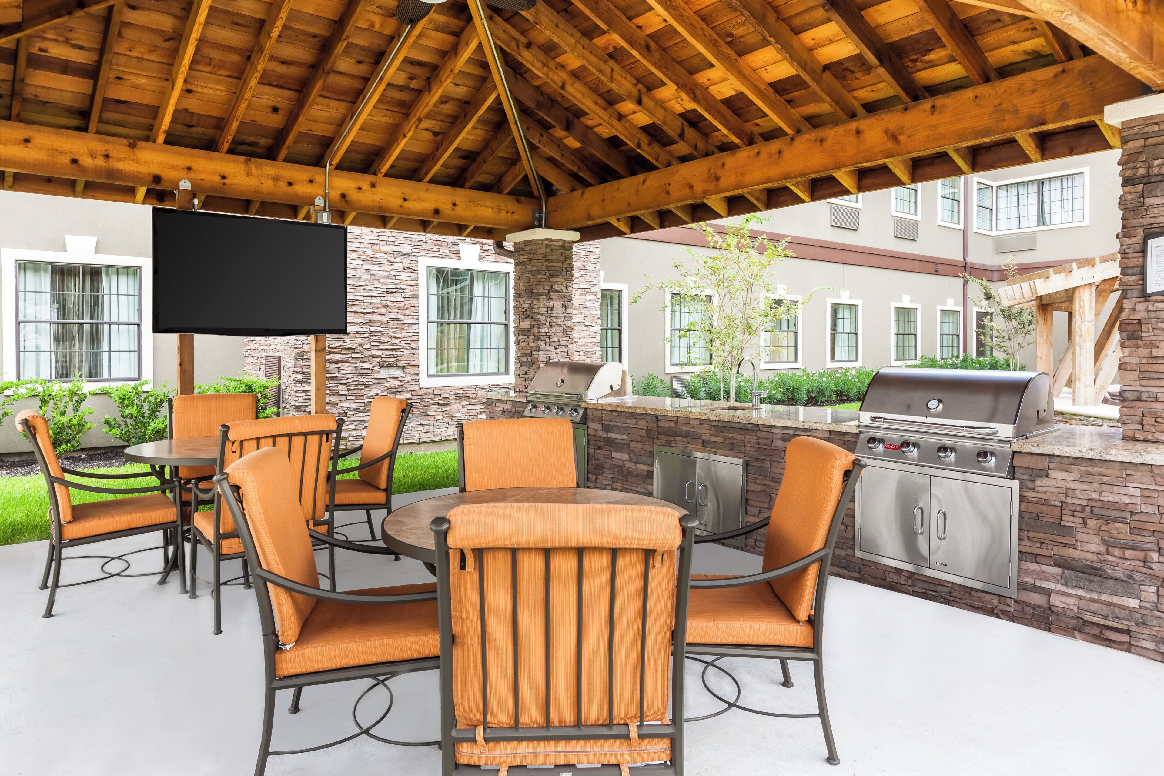 Un patio al aire libre con una mesa redonda y sillas, una parrilla y una pantalla de televisión.