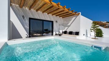 A modern outdoor pool area with a wooden pergola, a seating area with cushions, and a glass door leading to a covered space.