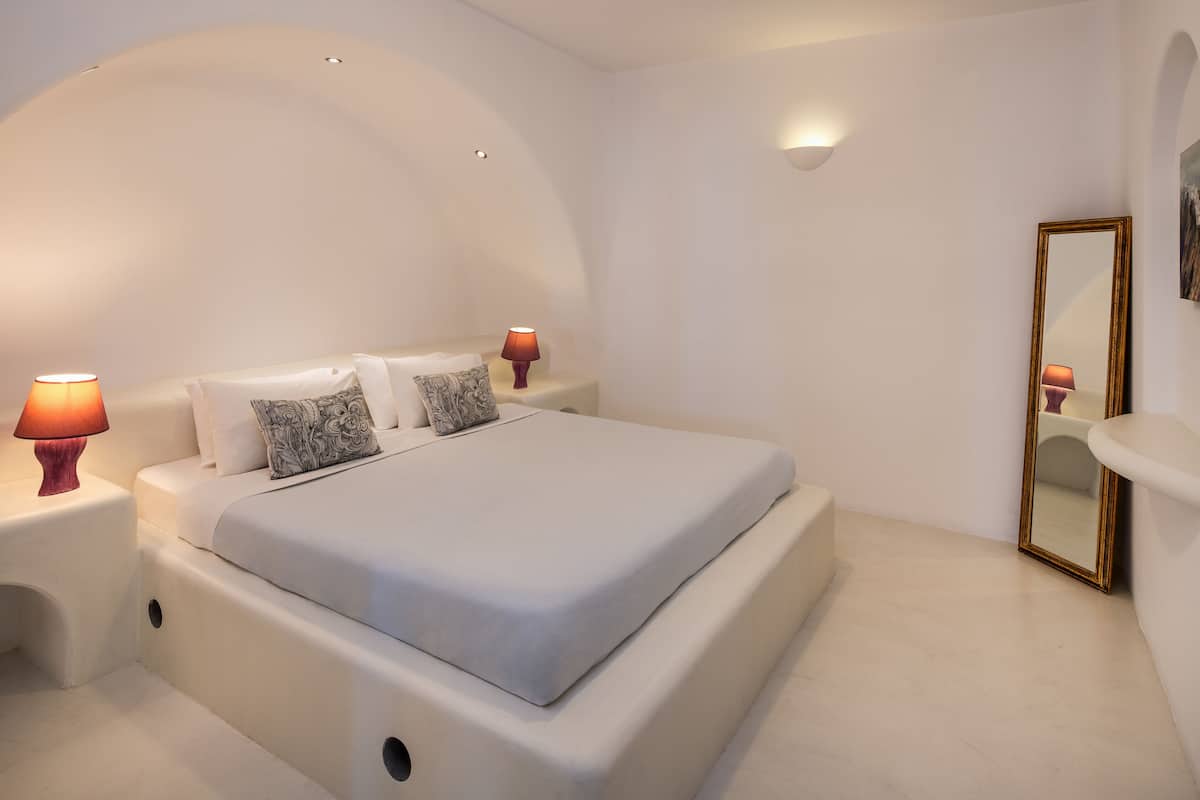 A modern bedroom with a large bed, two bedside lamps, a mirror, and a white wall.