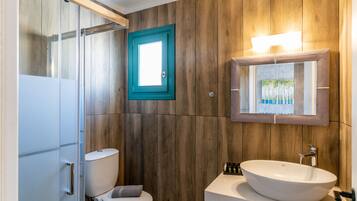 Une salle de bain avec un mur en bois, des toilettes blanches, un lavabo blanc et un miroir avec une lumière au-dessus.