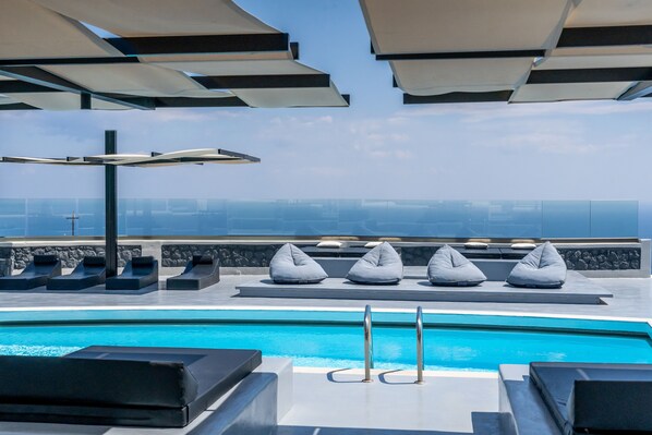 A rooftop pool area with lounge chairs and umbrellas, offering a view of the city skyline. - Abrazo Villas (Santorini)