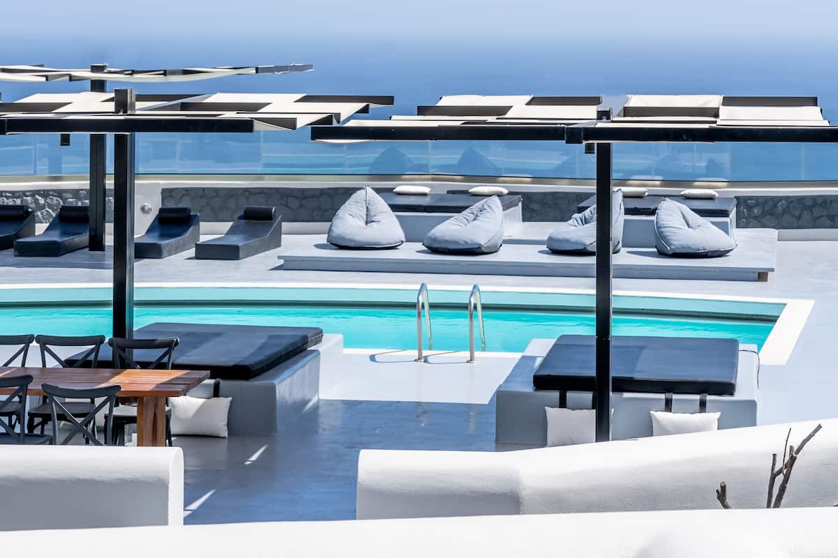 A rooftop pool area with lounge chairs, a table, and a view of the ocean.