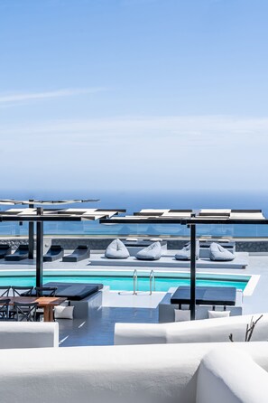 A rooftop pool area with lounge chairs, a table, and a view of the ocean. - Abrazo Villas (Santorini)