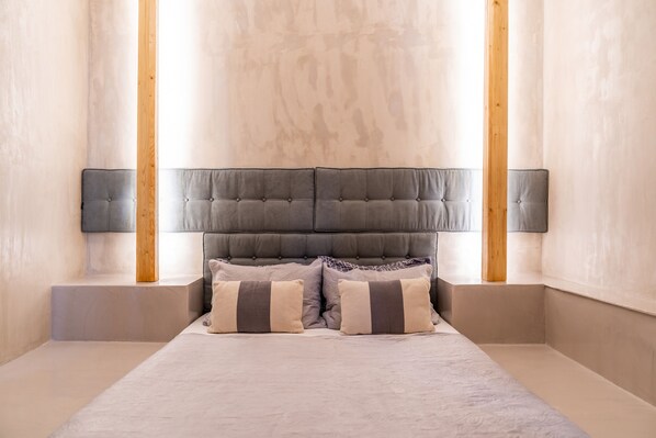 Une chambre à coucher moderne avec une tête de lit capitonnée, deux lampes de chevet et une palette de couleurs neutres.