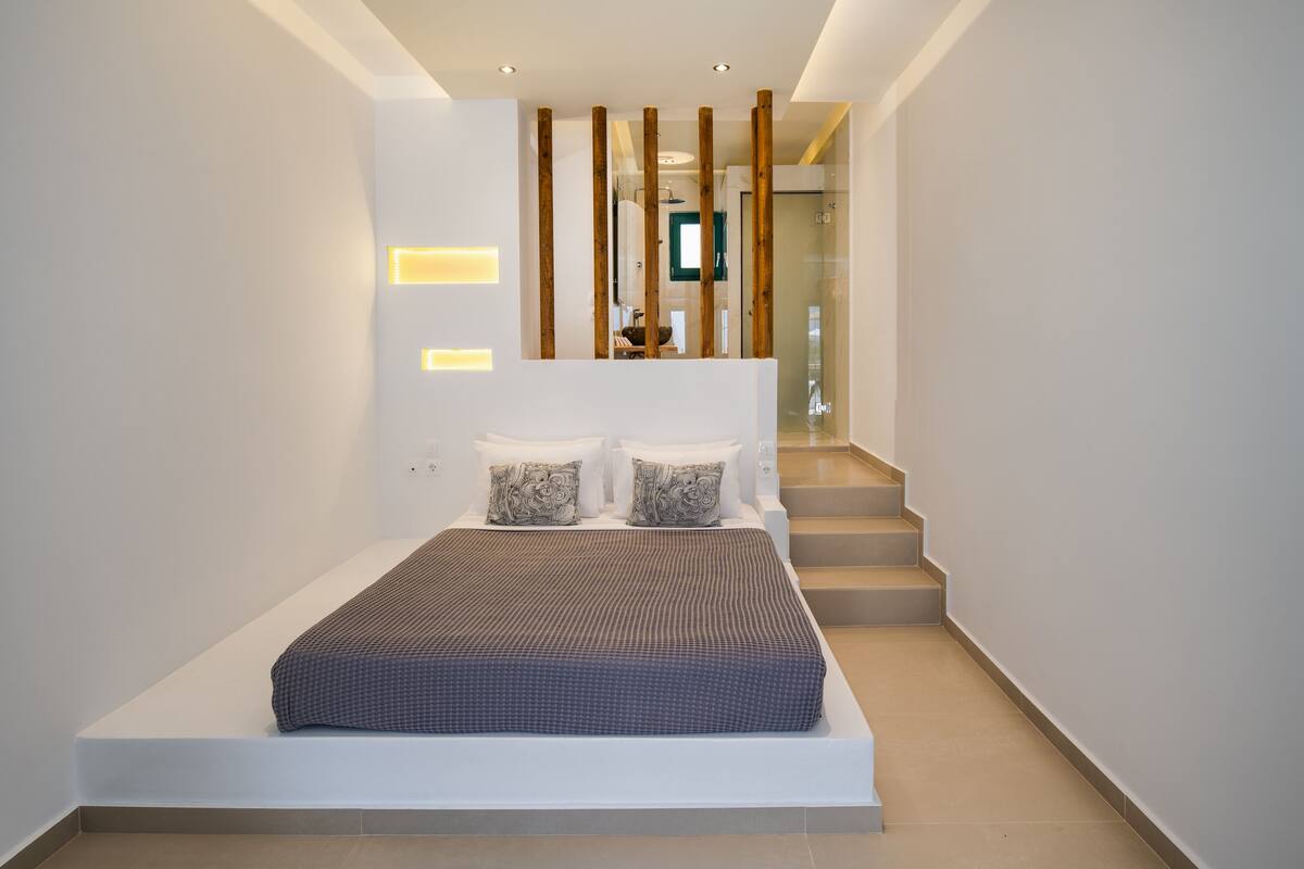 A modern bedroom with a large bed, a wooden partition, and a staircase leading to an upper level.