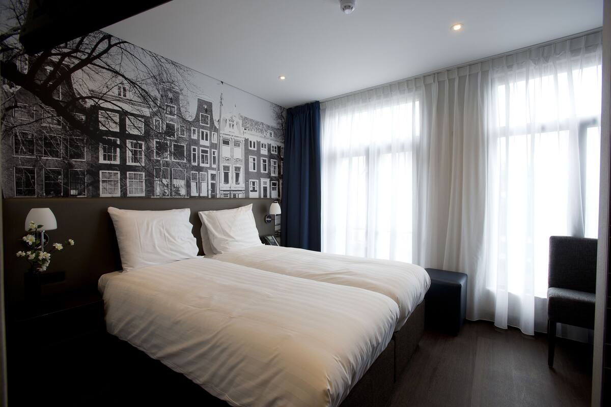 A hotel room with a large bed, a chair, a small table, and a wall mural.