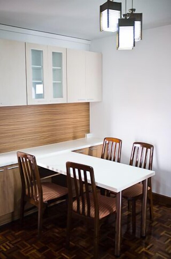 A compact kitchen with white cabinets, a wooden countertop, and a dining table with four chairs.