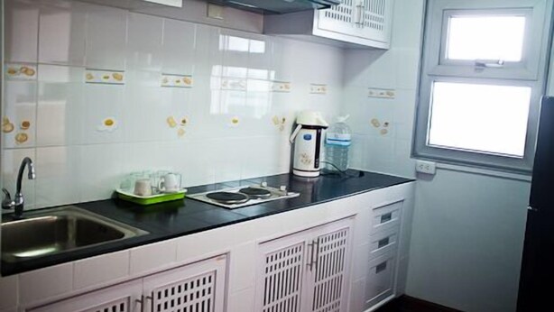 Cocina con armarios blancos, encimera negra, un lavamanos y una tetera, además de una ventana.