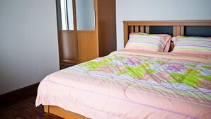 Un dormitorio con cabecera de cama de madera, colcha rosa y almohadas a rayas.